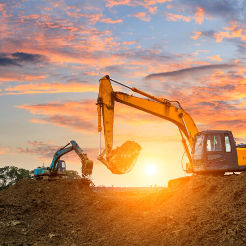 Three excavators work on construction site at sunset